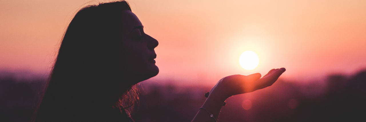 A woman with her hand out at sunset.