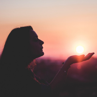 A woman with her hand out at sunset.