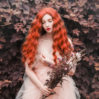 Woman with curly red hair with a tulle dress in a garden, holding flowers.