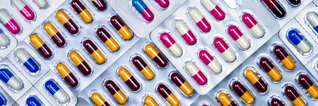 Being Shamed for Taking Medication as a Person With Chronic Illness Assortment of colorful pills in blister packs.