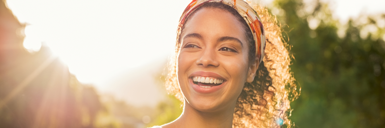 Young woman of color smiling and looking away at park during sunset. Happy outdoors
