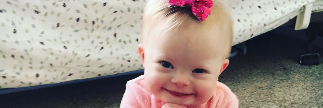 Ann's daughter who has Down syndrome wearing a pink onesie and bow in her hair.