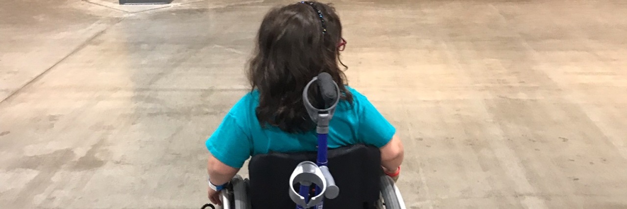 view of the back of a girl in a wheelchair, crutches attached to chair