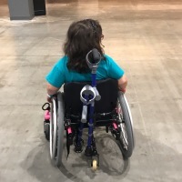 view of the back of a girl in a wheelchair, crutches attached to chair
