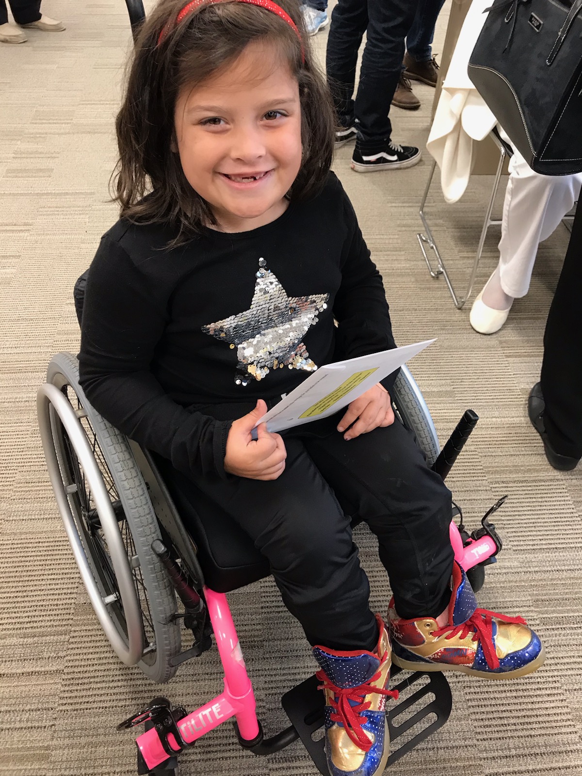 Amys daughter sitting in her pink wheelchair, smiling.