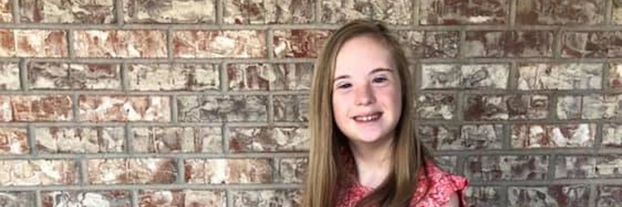 To the OBGYN Who Said My Child With Down Syndrome Would Be a 'Burden' Girl with Down syndrome smiling at camera with arms crossed