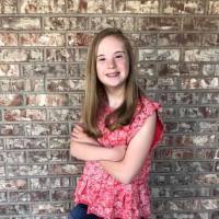 Girl with Down syndrome smiling at camera with arms crossed