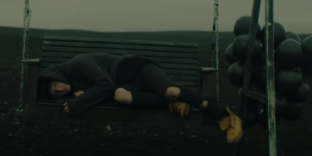 screenshot from NF song The Search, with rapper lying on swing on desolate landscape with black balloons blowing around him