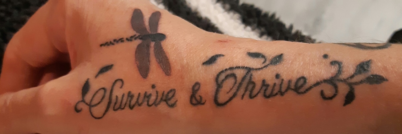 Jennifer's hand tattoo which reads "Survive and Thrive" and a dragonfly on it.