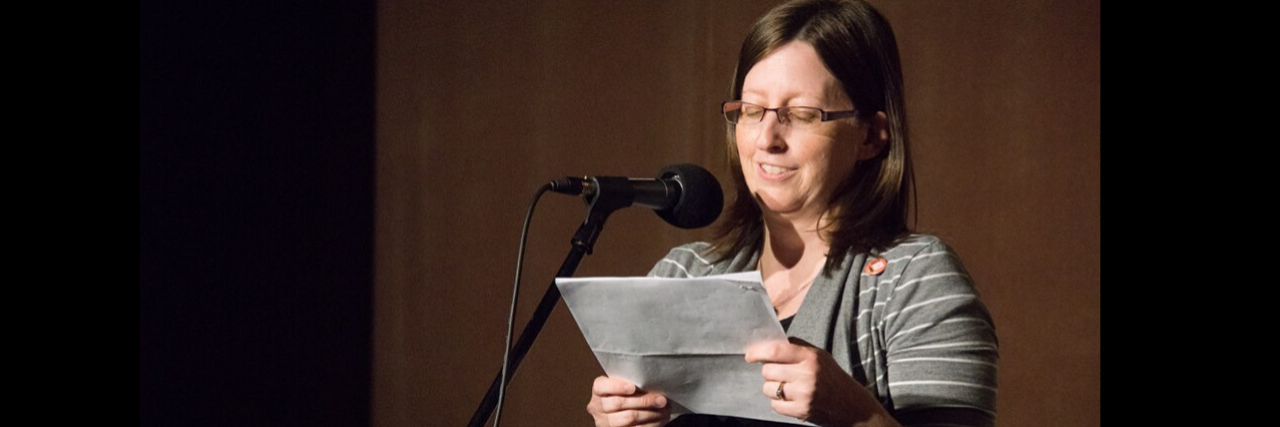 Reclaiming My Life With Huntington’s Disease A woman stands onstage reading during a live event.