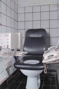 It's an image of a toilet seat with a computer, keyboard, telephone, and fax machine attached.