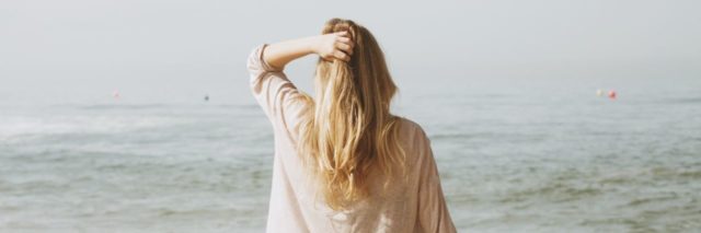 photo of woman at beach with hand in hair and looking out to sea