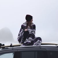 Girl on top of a car wrapped in a blanket looking ro the right. White background, red beanie, long hair
