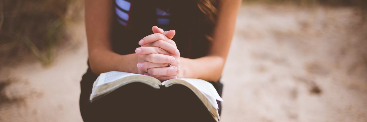 Living With Chronic Illness and Trauma: What to Know focus on woman sitting on a log with her hands folded over a book