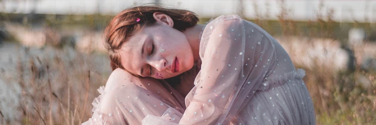 What You Need to Know About Being Young and Having Chronic Pain photo of woman sitting by ocean in white dress hugging knees