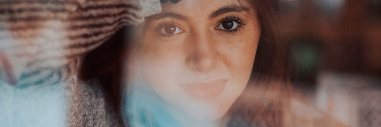 photo of young woman looking anxious through window