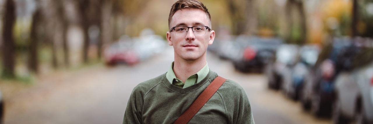 photo of man with shoulder bag standing in middle of road looking at camera