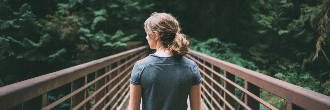 Why You Shouldn't Judge People With an Addiction photo of woman in forest standing on bridge, facing away from camera