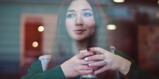 The Surprising Link Between My Digestive Disease and My Eating Disorder photo of dark haired young woman in coffee shop with coffee and croissant