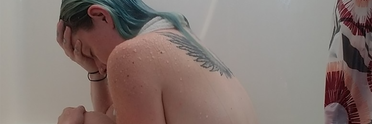 Recording My Thoughts During a Migraine Episode photo of contributor, a woman with green coloured hair, sitting in bath with hand resting on forehead