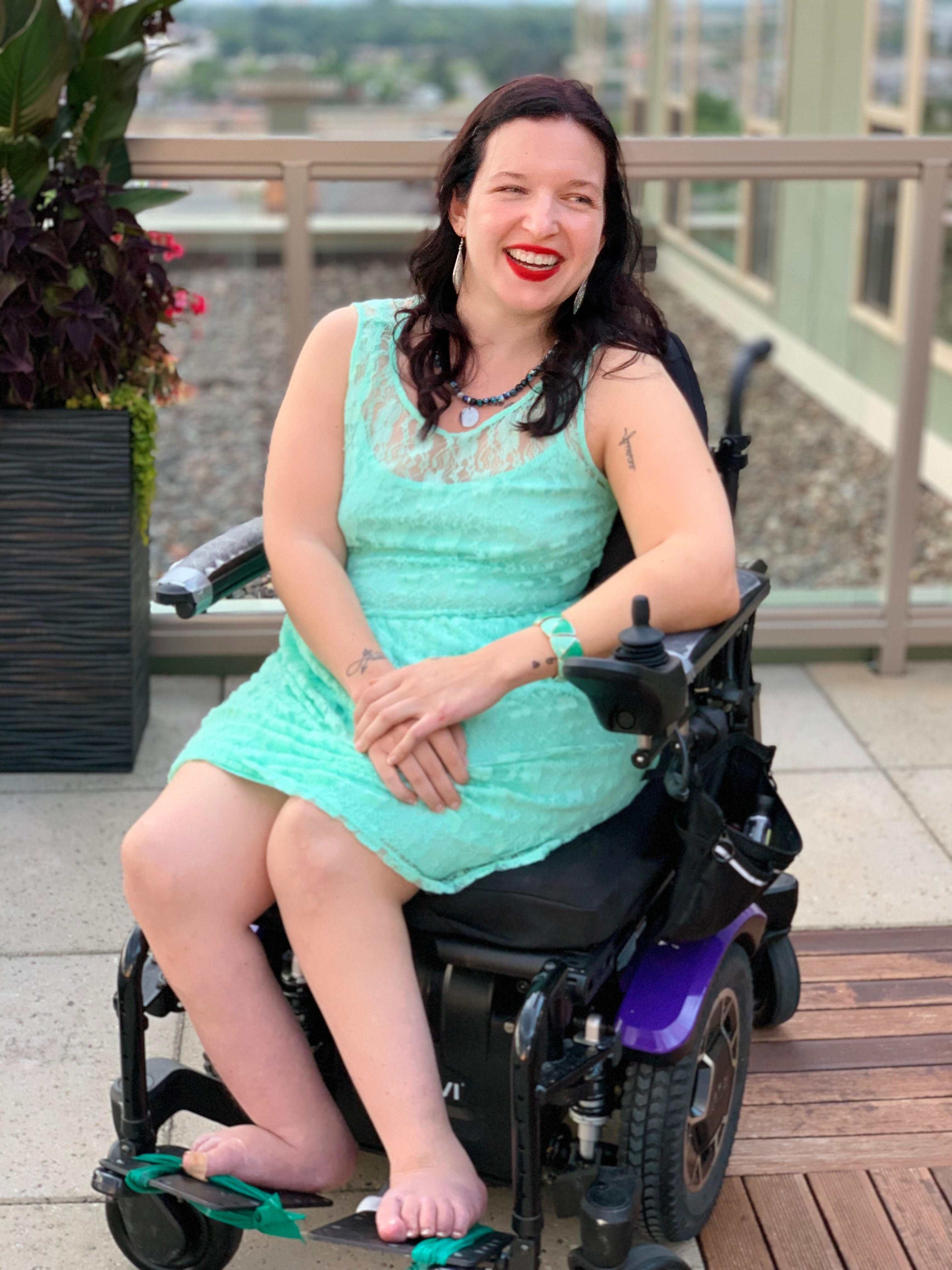 Mollie smiling. She is sitting in her power wheelchair and wearing a bright turquoise dress.