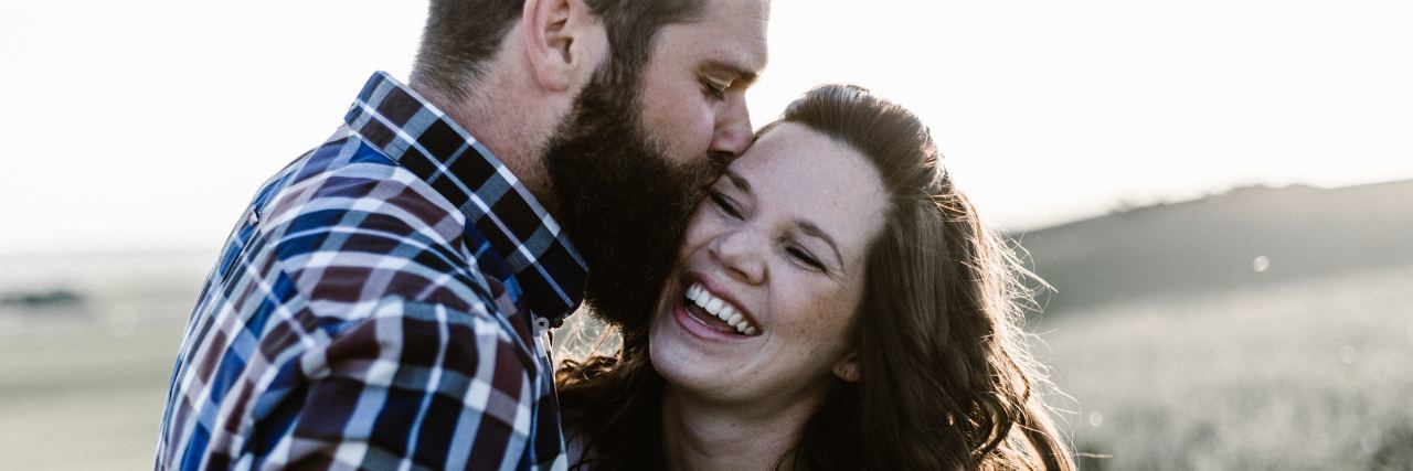 photo of man kissing woman's cheek in field. woman is smiling with eyes closed