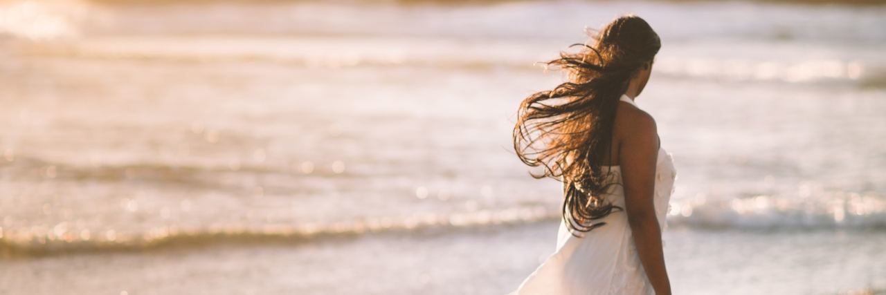 photo of woman in white dress walking alone beach in golden light