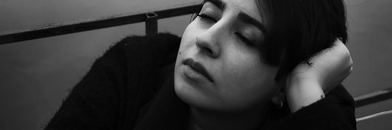 When You're Grieving the Person You Were Before Chronic Fatigue black and white photo of young woman sitting by lake looking upset or tired