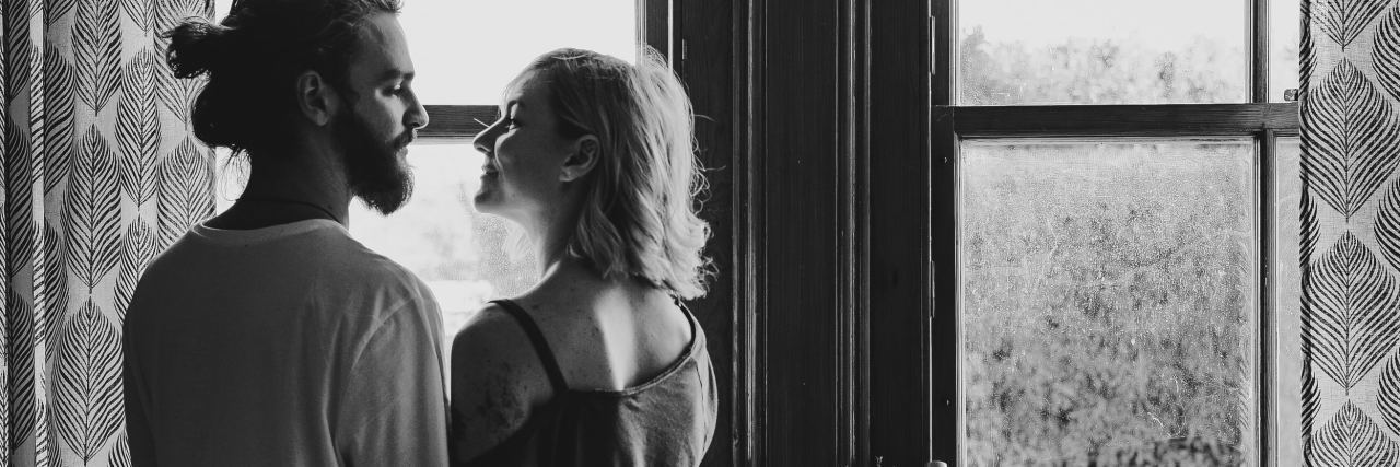 The Biggest Lesson I Learned in Marrying Someone With a Chronic Illness black and white photo of young couple looking into each others' eyes by window