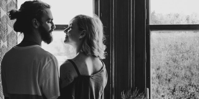 black and white photo of young couple looking into each others' eyes by window