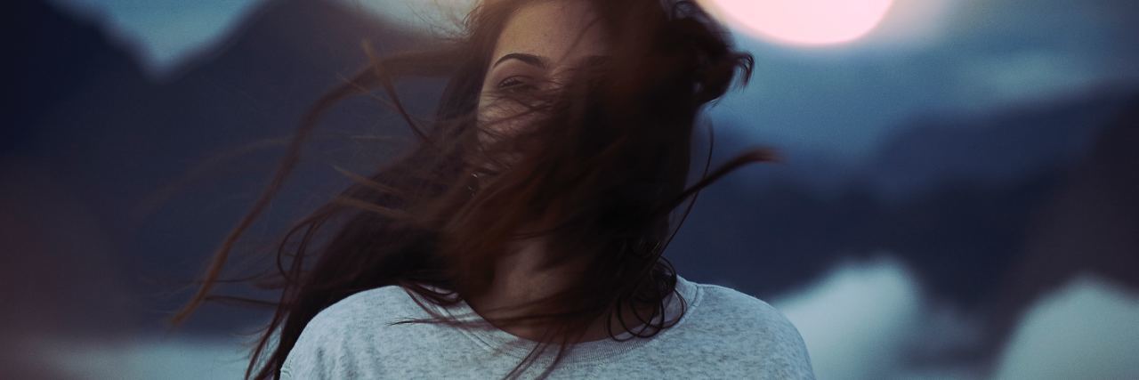 What Someone With Ehlers-Danlos Syndrome Keeps Hidden From Others photo of woman with blurry background of lights and dark hair covering her face