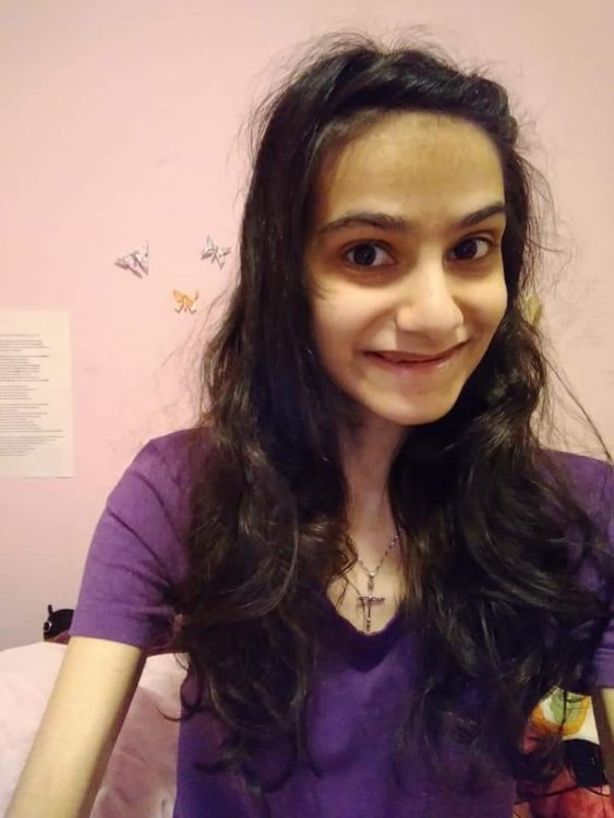 woman with purple shirt and long hair smiling while looking at camera