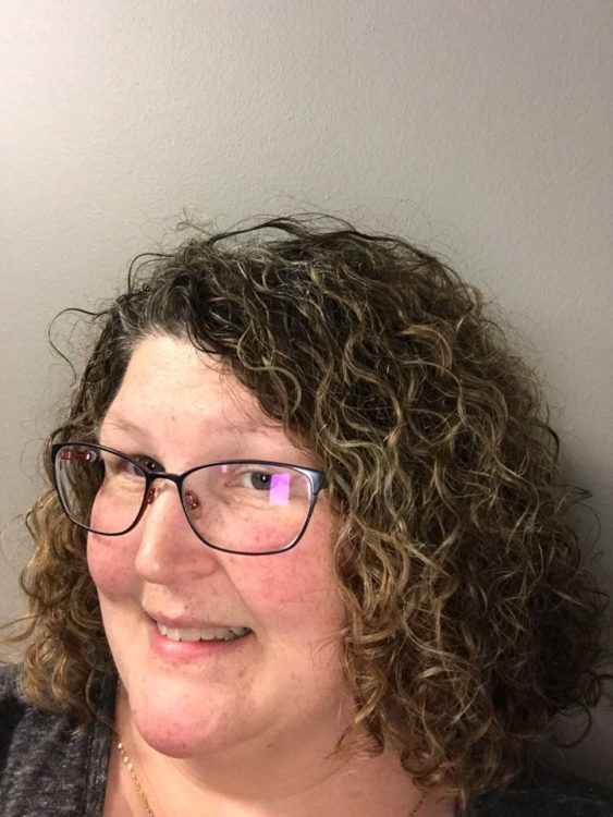 woman with curly hair and glasses smiling