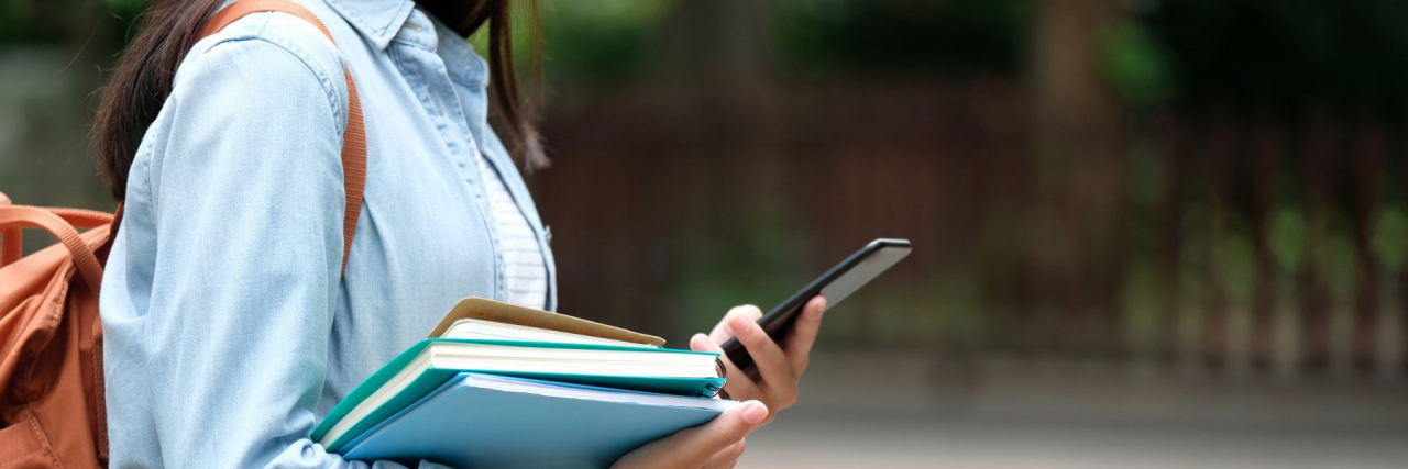 Cropped shot of a woman holding books and phone with a backpack