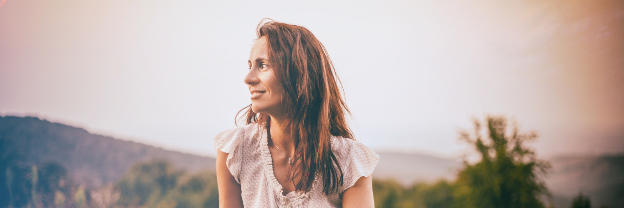 Saying You're Fine When You're Not When Chronically Ill Woman sitting on a fence outdoors.