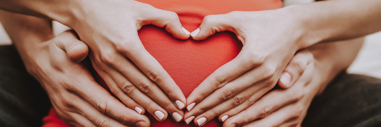 Unfollowing Pregnant Friends and Family After a Miscarriage A woman forms a heart over her pregnant belly.