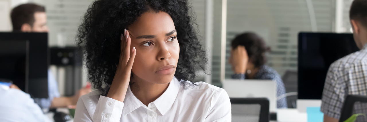 How a Stressful Corporate Job Affected Anxiety and Suicidal Thoughts photo of woman sitting at office desk looking stressed with hand raised to head
