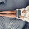 Young woman using laptop, relaxing in her bed