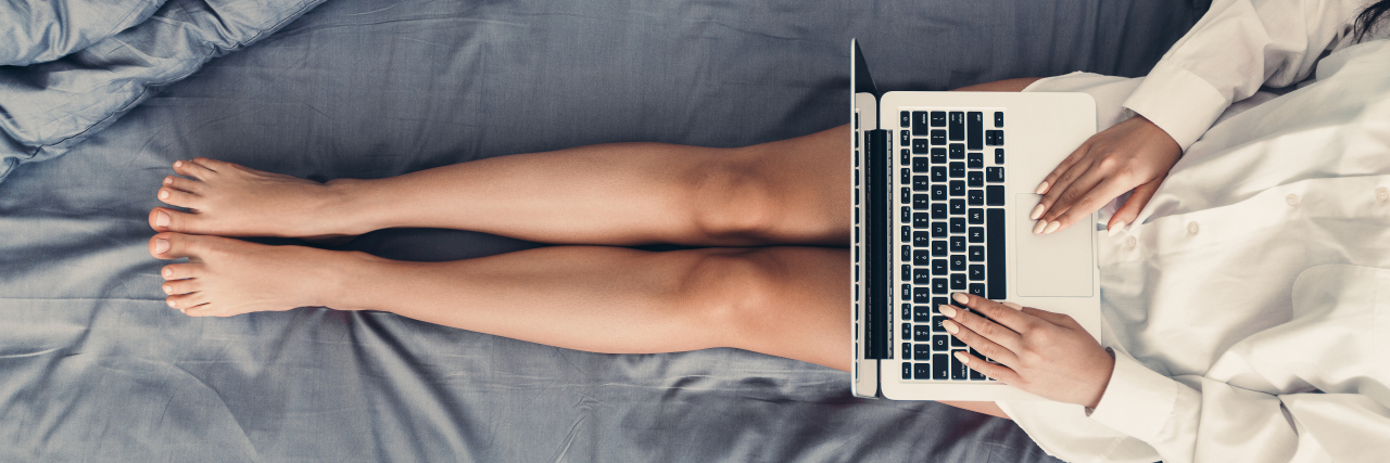 Young woman using laptop, relaxing in her bed