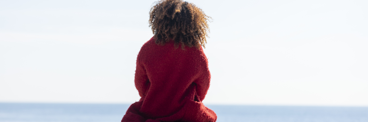 Making Hard Choices in Life With Chronic Pain and Illness Woman with curly hair sitting on a bench at the beach.