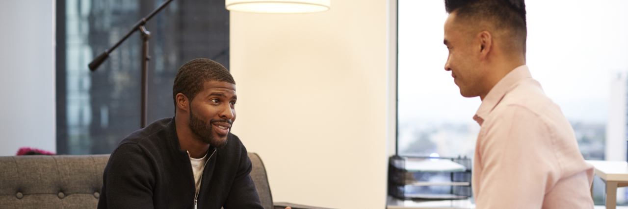 Man Sitting On Couch Meeting With Male Counsellor In Office