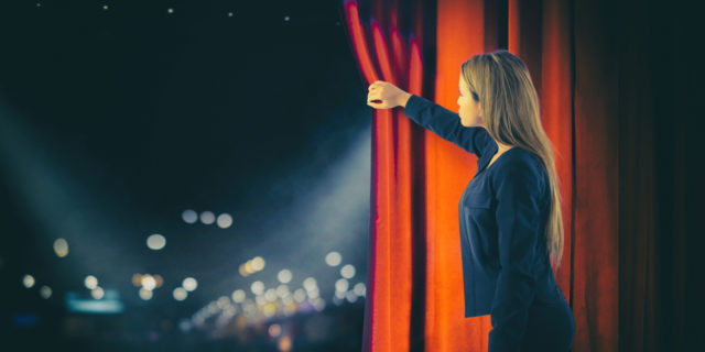 Woman opening red curtains on theater stage.