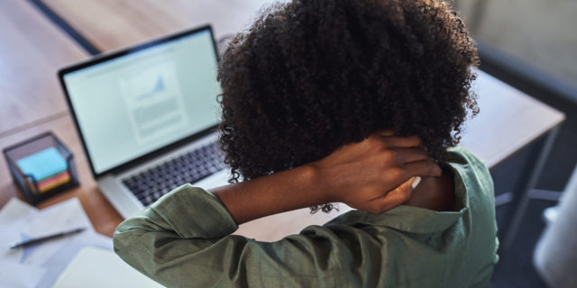 The Mistakes I Made While Working Full-Time With an Invisible Illness woman rubbing her neck while sitting in front of a computer at a desk