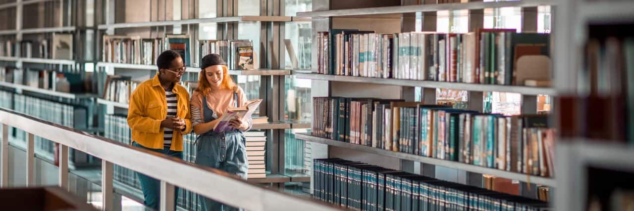 Two students talking about a book in the library