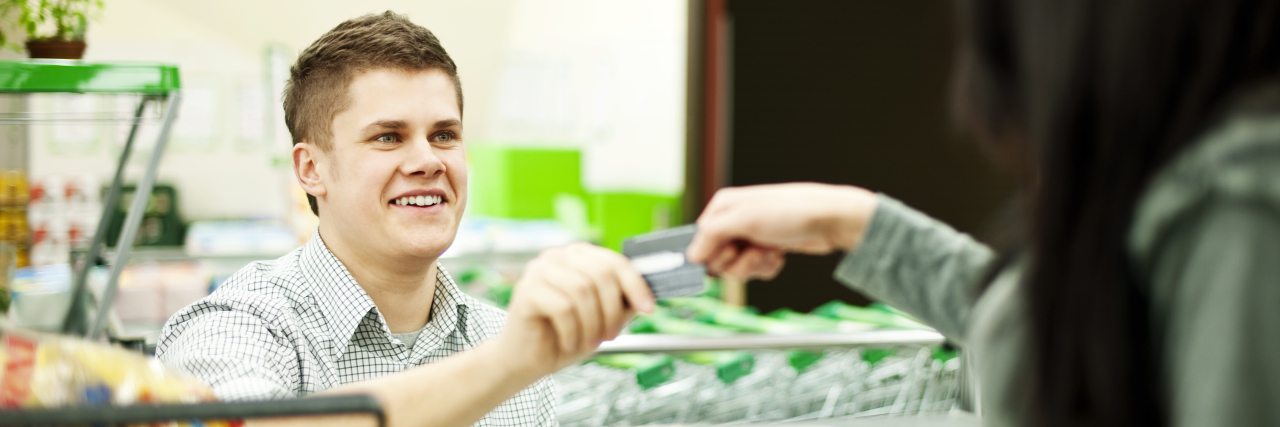 Young man helping woman at grocery checkout.