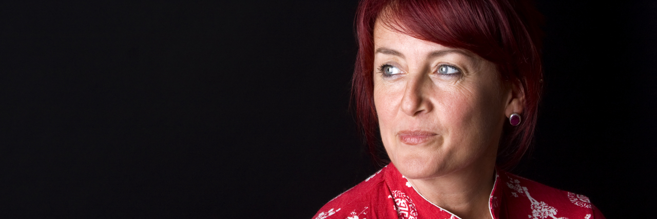 Middle aged woman with red hair looking into the distance. Wearing a red shirt with white print