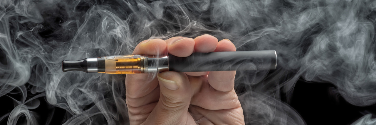 KHN: Meet the Health Officials Who Alerted the World to Vaping Illness Hand holding an electronic cigarette over a dark background
