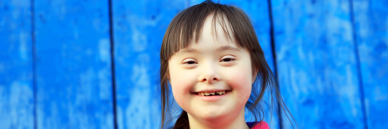 Girl with Down syndrome smiling. Blue wall in background.