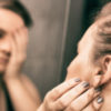 A woman looking in the mirror and holding her head