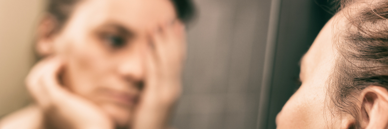 What Depression Looks, Feels and Sounds Like To Me A woman looking in the mirror and holding her head